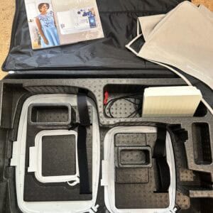 Open travel case showing organized compartments and instruction manuals on top — likely for sewing machines or equipment accessories.