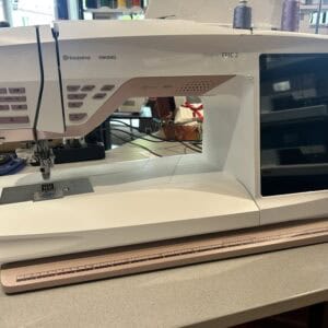 Husqvarna Viking Epic 2 sewing machine on a counter with a brown ruler in front and fabric kept to the side.