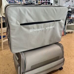 Large gray Husqvarna Viking sewing machine case on a wheeled cart in a sewing shop.