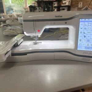 Industrial sewing machine (Brother Celeste) with touchscreen showing embroidery pattern grid on the right in a craft shop setting