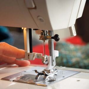 Close-up of a sewing machine needle and presser foot guiding fabric under the needle by a hand.