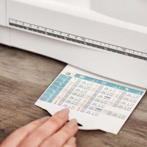 Close-up of a hand flipping through a blue-and-white chart on a wooden desk, with a white measuring device nearby.