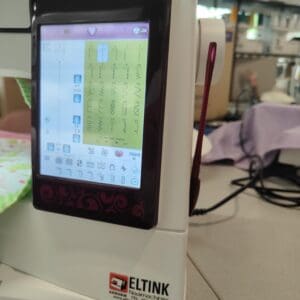 Close-up of a sewing machine touchscreen displaying stitch patterns on a colorful grid, with 'Designer Ruby Royale' branding above the screen.