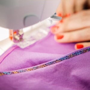 Close-up of a sewing machine stitching a purple fabric with a beaded edge.