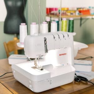 White Bernina L 650 sewing machine on a wooden table with multiple thread spools, in a sewing room setting.
