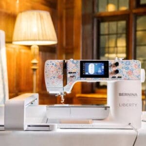Bernina Liberty sewing machine with a floral pattern on a table in a warmly lit room, ready to stitch.