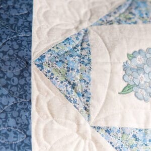 Quilt block featuring blue floral fabrics arranged in a triangle on a white quilt with decorative stitching patterns.