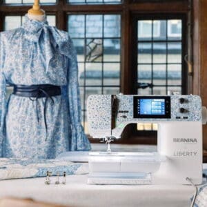 Blue floral dress on a mannequin beside a Bernina Liberty sewing machine at a sewing table.