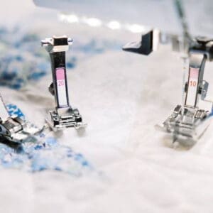 Close-up of sewing machine presser feet on white fabric with blue floral pattern and measurement marks during stitching
