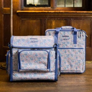 Two blue floral travel bags with zippers and blue trim sit on a wooden floor, one showing a front pocket and the other a side view (Bernina Liberty).