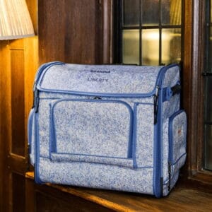 Blue speckled sewing machine travel case with handles, labeled Bernina Liberty, placed on a wooden doorstep near a window.