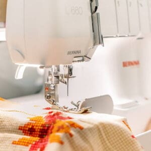 White Bernina sewing machine stitching a floral orange-red fabric up close.