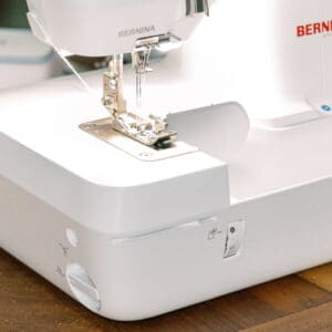 Close-up of a white Bernina sewing machine with needle and presser foot on a wooden table.