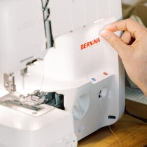 Person threads a Bernina sewing machine, guiding thread from the needle area on a white fabric-less machine surface