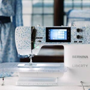 Floral-patterned Bernina Liberty sewing machine on a table with fabric pieces and spools nearby, ready to sew