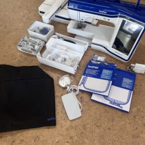 IMG_4112 - Eltink Naaimachines Blue and white Brother Innov-is XV sewing/embroidery machine with accessories laid out around it on a floor, including boxes and trays of parts.