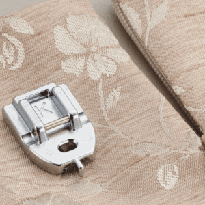 Close-up of a silver metal zipper slider resting on patterned beige fabric with floral motifs.
