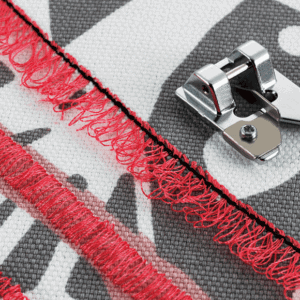 Close-up of a red zipper being sewn onto fabric with a metal zipper foot nearby.