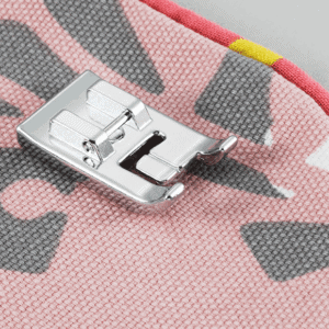 Close-up of a metal sewing machine presser foot resting on pink camouflage-patterned fabric.