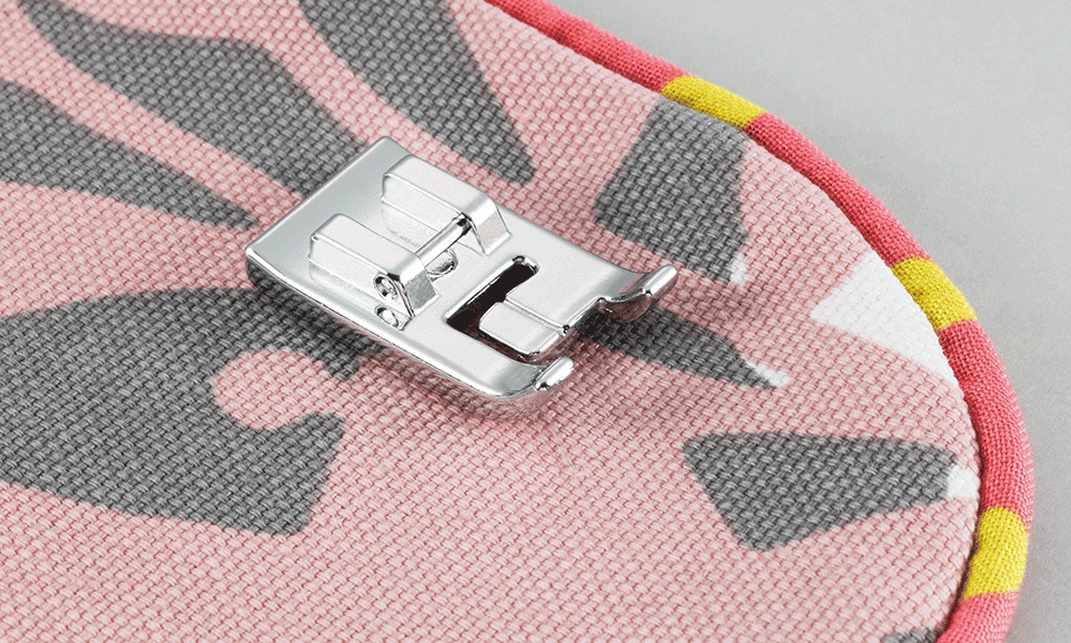 Brother Paspelvoet F067 - Eltink Naaimachines Close-up of a metal sewing machine presser foot resting on pink camouflage-patterned fabric.