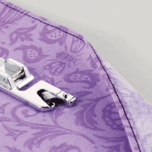 Close-up of a silver zipper slider on lavender patterned fabric.