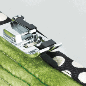 Close-up of a sewing machine presser foot attaching a polka-dotted strap to green fabric.