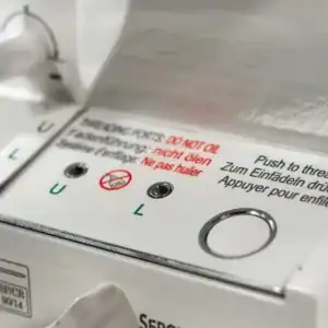 Close-up of a sewing machine control panel with threading instructions in multiple languages saying 'Push to thread' and a circular button.